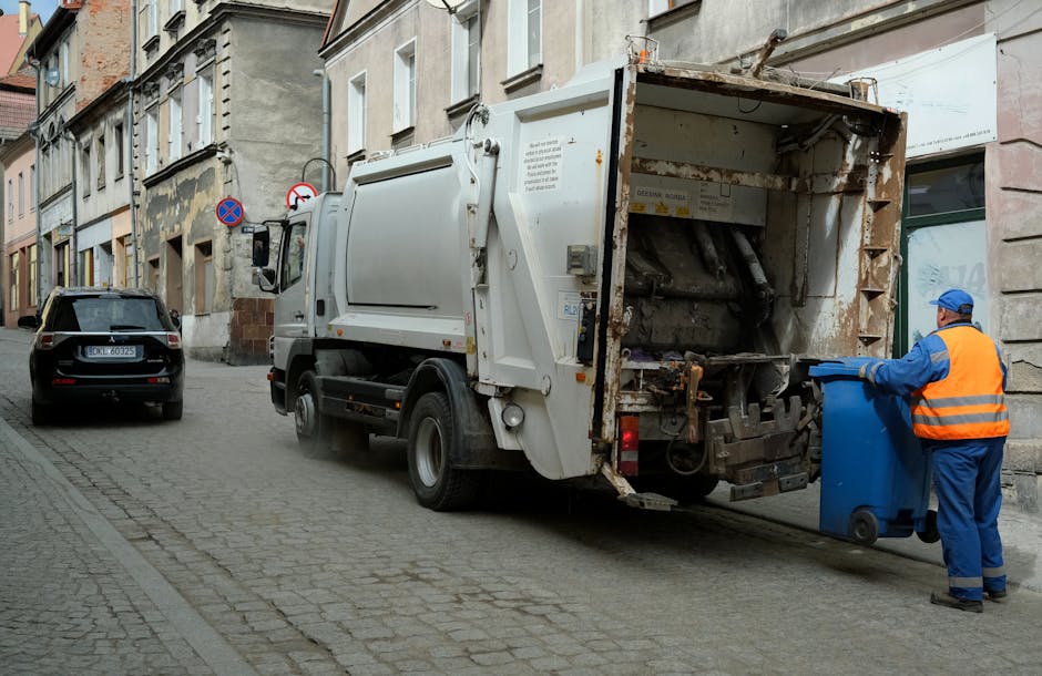 A large pile of black rubbish bags, some partially torn, are stacked against a tiled wall on an urban street or outdoor area. Several transparent plastic bottles, including water bottles, are scattere